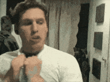 a man in a white shirt adjusts his tie in front of a mirror