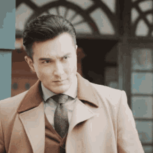 a man wearing a tan coat and tie looks to his left