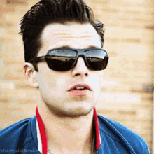a young man wearing sunglasses and a blue jacket is looking at the camera .