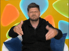 a man in a black jacket is making a funny face in front of a colorful background