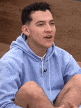 a young man in a blue hoodie is sitting on a wooden floor .