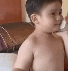 a shirtless young boy is eating an ice cream cone in a bedroom .