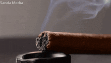 a close up of a cigar in an ashtray with sanda media in the corner