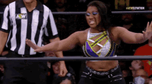 a female wrestler is standing in a ring with her arms outstretched in front of a referee .