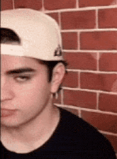 a man wearing a baseball cap and a black shirt is standing in front of a brick wall .