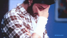 a man wearing a plaid shirt is covering his face