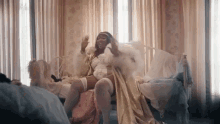 a woman in a fur robe is sitting on a bed in a room .