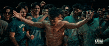 a shirtless man stands in front of a crowd with the word kahar on the bottom right