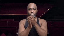 a bald man with a beard wearing a black tank top and a necklace with the letter t on it