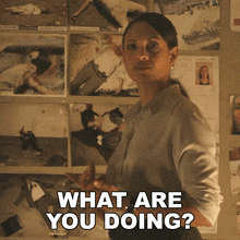 a woman is standing in front of a wall with pictures and the words " what are you doing "