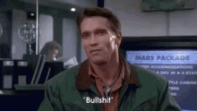 arnold schwarzenegger is wearing a green jacket and a red shirt and is talking to someone .
