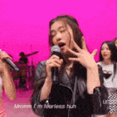 a woman is singing into a microphone on a pink background while making a funny face .