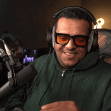 a man wearing headphones and sunglasses is sitting in front of a microphone with his hands folded