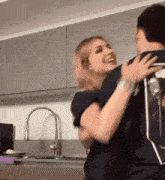 a man and a woman are hugging each other in a kitchen in front of a sink .