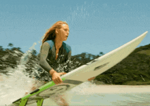 a woman in a wetsuit is holding a surfboard with the letter g on it
