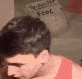 a man in a red tank top is standing in front of a to-do list .