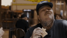 a man with a tattoo on his neck is eating a sandwich in a restaurant .