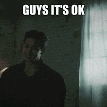 a man is smiling in a dark room with the words guys it 's ok below him