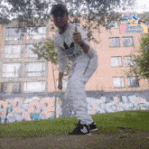 a man wearing an adidas shirt gives a thumbs up in front of a building with graffiti on it