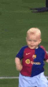a young boy wearing a red and blue nike shirt is running on a field
