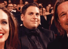 a man in a tuxedo and bow tie is sitting next to a woman and a man in a suit .
