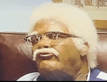 a man wearing glasses and a fake mustache is sitting on a couch .