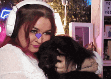 a woman wearing headphones holds a black dog with a purple heart on her nose