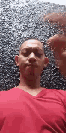 a man in a red shirt is making a face in front of a black wall .