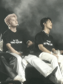 a man wearing a black shirt that says say 10 hung huynh sits next to another man