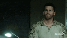 a man in a military uniform is standing in a dark room with a lamp in the background .
