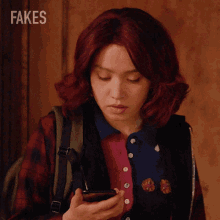 a woman with red hair is looking at her phone and the word fakes is behind her