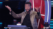 a man sitting at a podium with his arms outstretched in front of a podium that says the voice