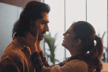 a woman touches a man 's face while they look into each other 's eyes