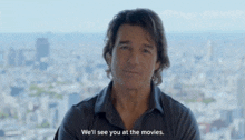 a man says " we 'll see you at the movies " in front of a city skyline
