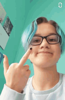 a girl with blue hair and glasses is pointing at her face