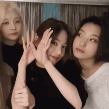 a group of three women are standing next to each other and making funny faces with their hands .