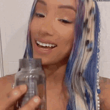 a woman with blue and white hair is smiling while holding a bottle .