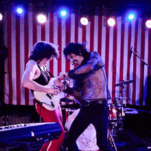 a man playing a guitar and another man playing drums on stage
