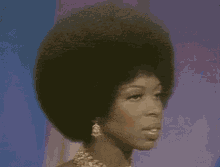 a woman with a big afro is wearing a gold necklace and earrings .