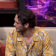 a man in a yellow shirt is sitting on a couch with a microphone in his mouth .