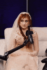 a woman in a wedding dress sits on a couch in front of a microphone