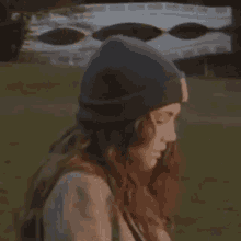 a woman wearing a beanie is standing in front of a bridge