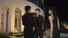 a woman in a black dress stands next to two men in suits