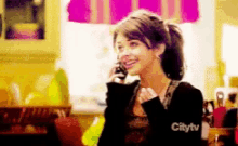 a woman is smiling while talking on a cell phone with citytv written on the bottom
