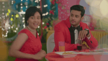 a man in a tuxedo and a woman in a red dress sit at a table