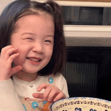 a little girl is smiling while holding a bowl with the letters a b c d e and f on it