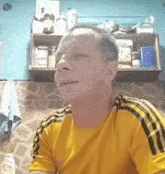 a man wearing a yellow shirt with black stripes on the sleeves is sitting in a kitchen with his eyes closed .
