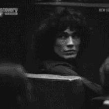 a man with curly hair is sitting in a chair in a dark room .