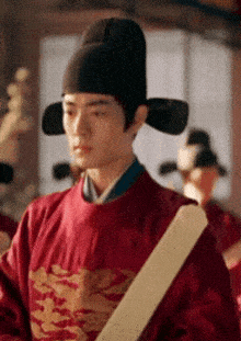a man wearing a red robe and a black hat is holding a sword .