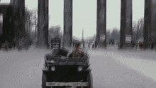 a man is driving a jeep down a snowy street in front of a very tall building .